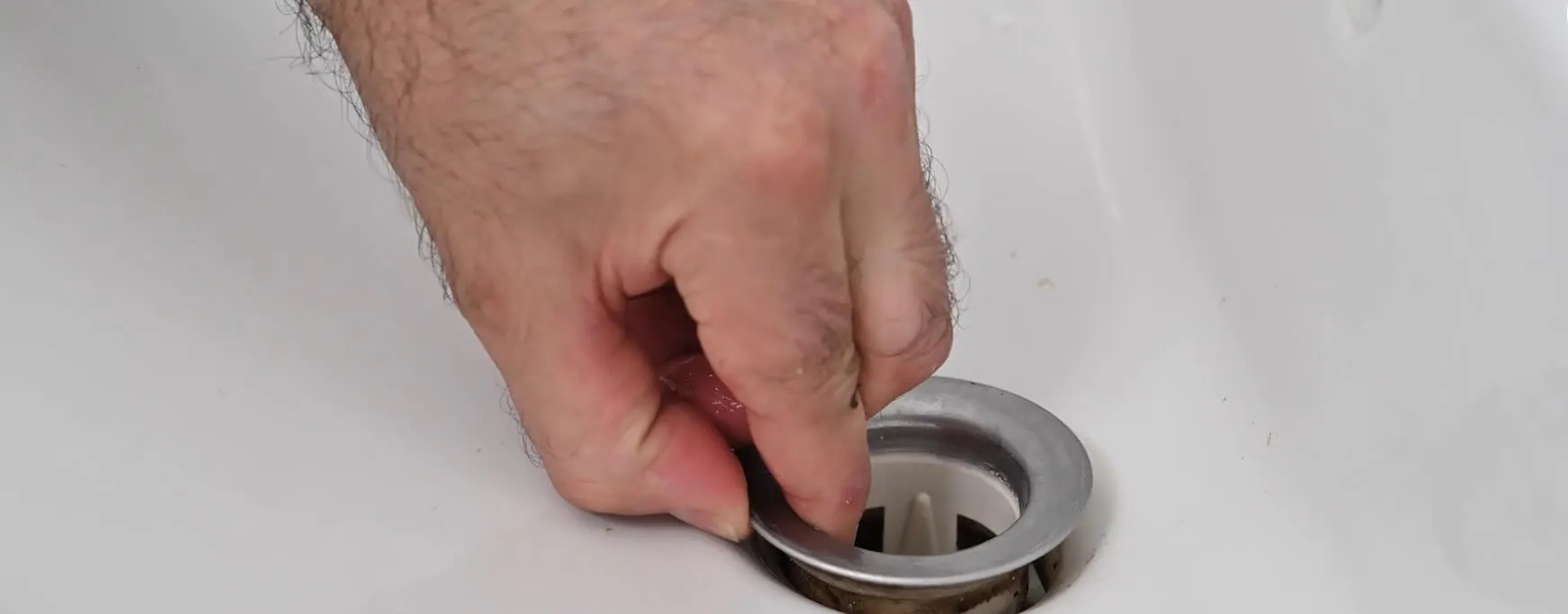 Main retirant la bonde usée d'un lavabo blanc pour la changer