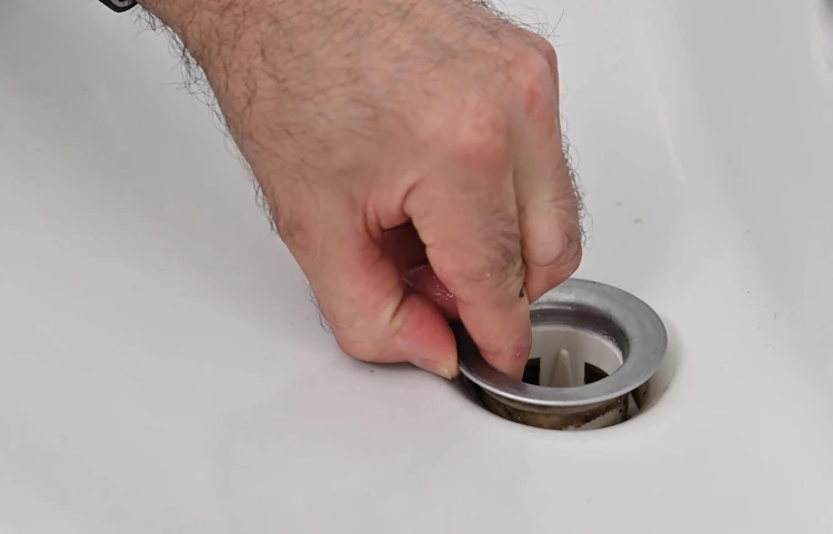 Main retirant la bonde d'un lavabo blanc