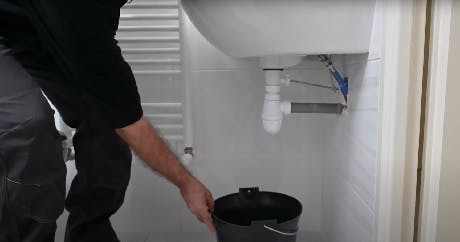 Plombier plaçant un seau sous un siphon de lavabo