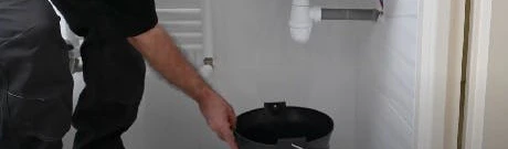 Plombier plaçant un seau sous un siphon de lavabo