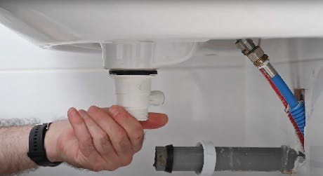 Main dévissant un raccord de siphon sous lavabo