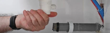 Main dévissant un raccord de siphon sous lavabo