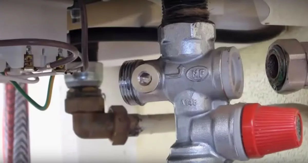 Groupe de sécurité NF installé sous un chauffe-eau avec soupape de surpression rouge