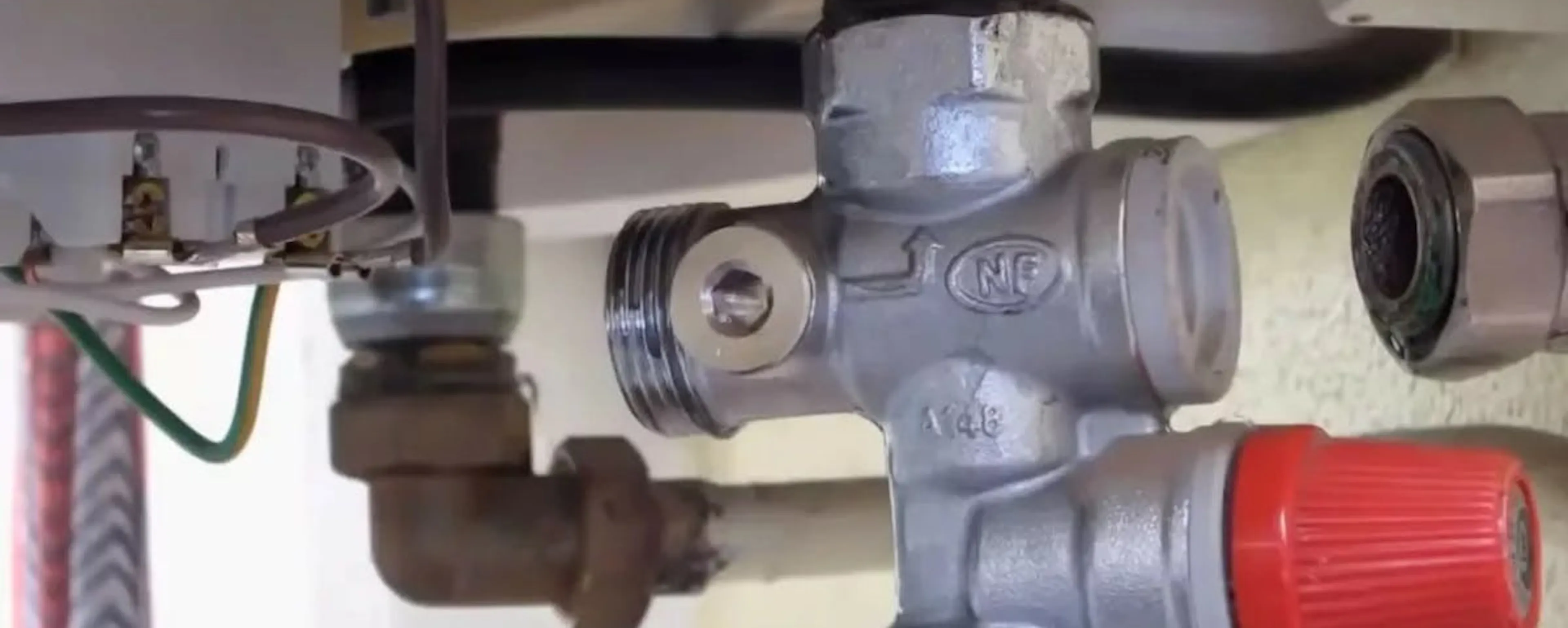 Groupe de sécurité NF possiblement à changer sous un chauffe-eau, avec soupape de surpression rouge