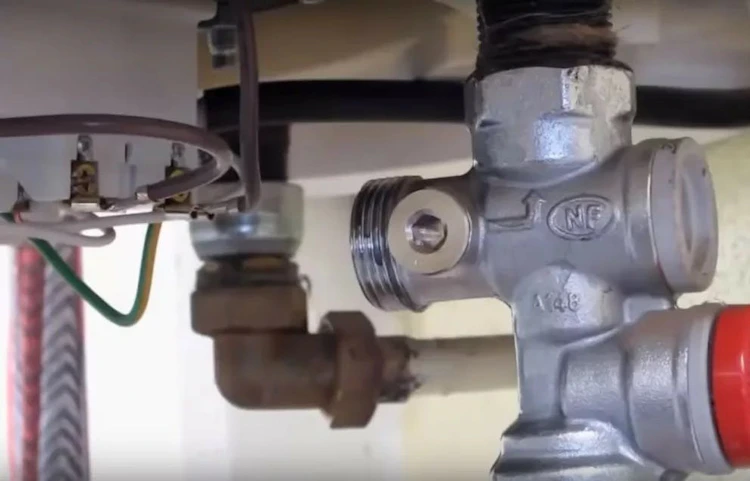 Groupe de sécurité NF installé sous un chauffe-eau avec soupape de surpression rouge