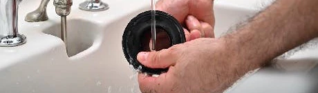 Mains rinçant le joint d'une bonde d'évier sous l'eau courante