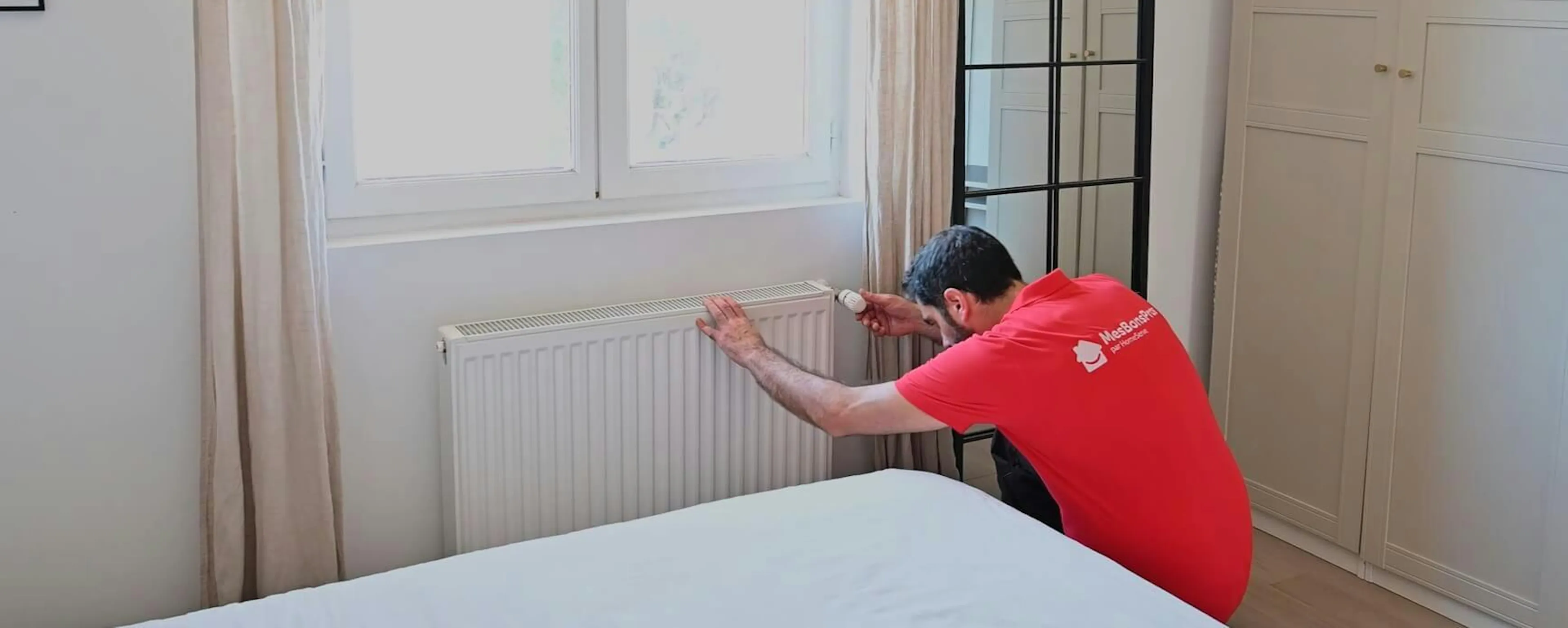 Technicien changeant le robinet d'un radiateur blanc sous une fenêtre