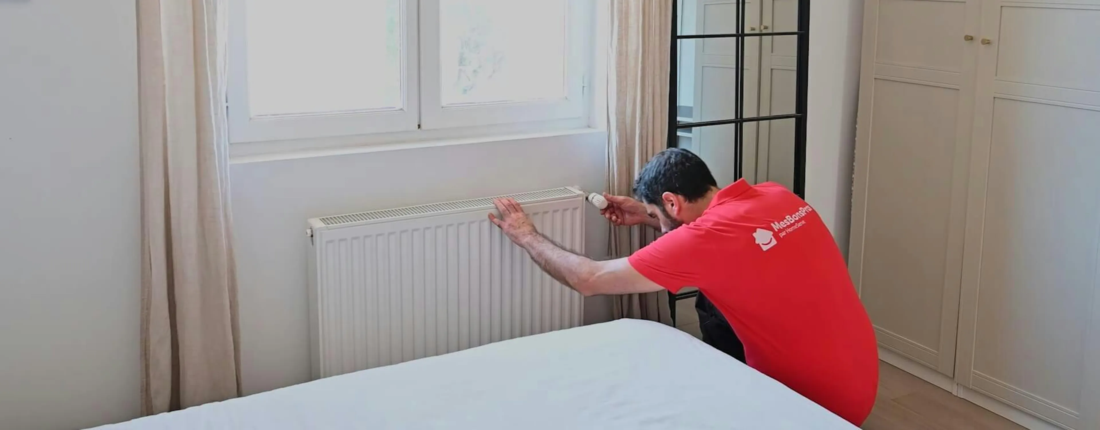 Technicien changeant le robinet d'un radiateur blanc sous une fenêtre