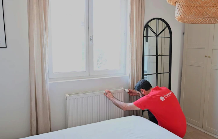 Technicien en rouge réparant un radiateur blanc sous une fenêtre