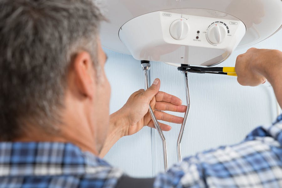 Homme âgé réparant un chauffe-eau électrique avec un tournevis