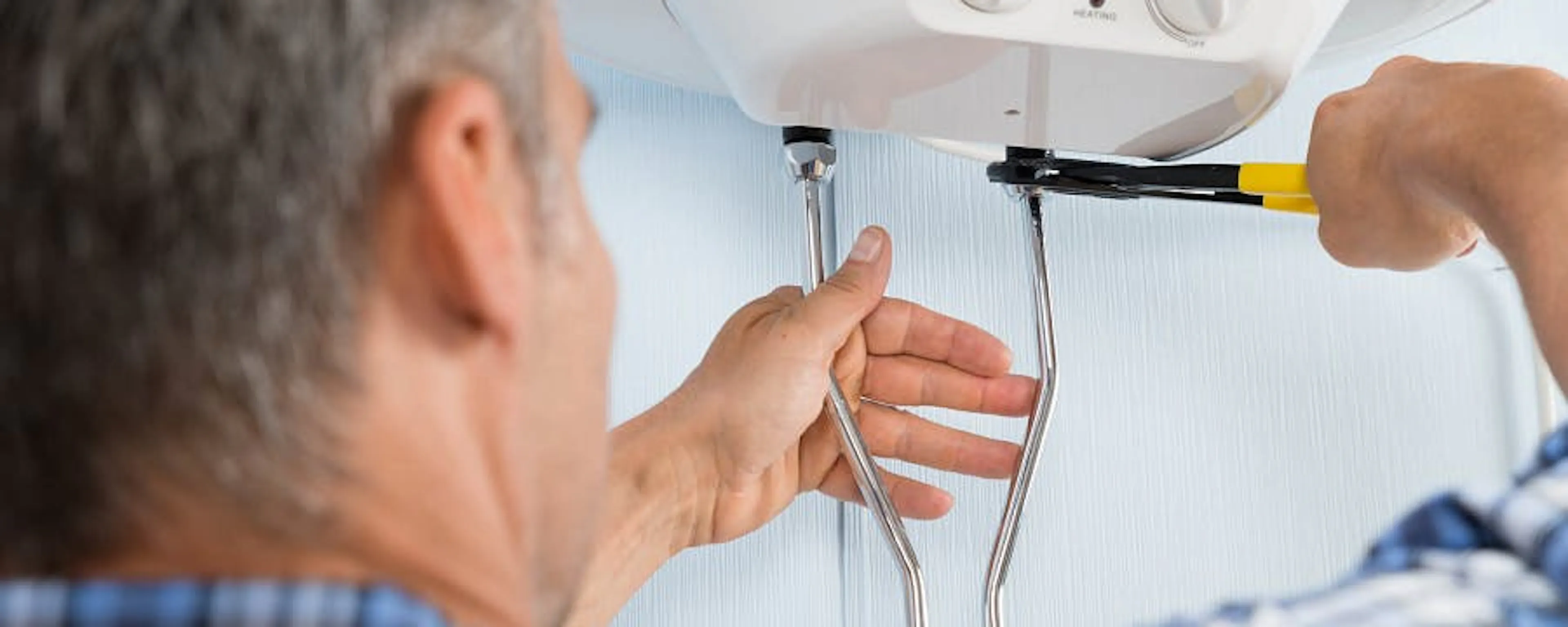 Homme âgé détartrant un chauffe-eau électrique avec un tournevis