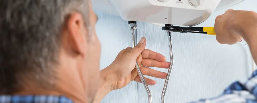 Homme âgé détartrant un chauffe-eau électrique avec un tournevis