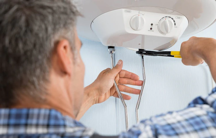 Homme âgé réparant un chauffe-eau électrique avec un tournevis