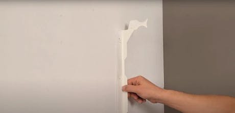 Main décollant du papier peint blanc d'un mur