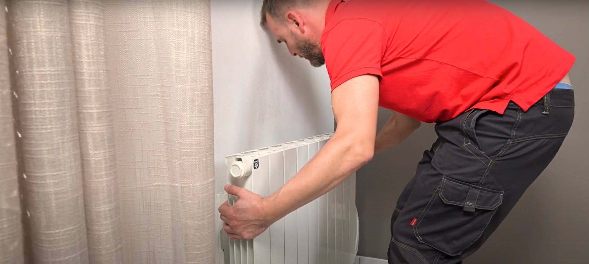 Technicien en rouge réglant le robinet d'un radiateur blanc
