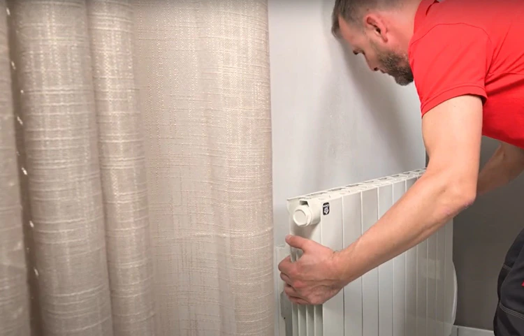 Technicien en rouge réglant le robinet d'un radiateur blanc