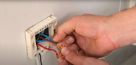 Main manipulant des fils électriques colorés dans une prise murale