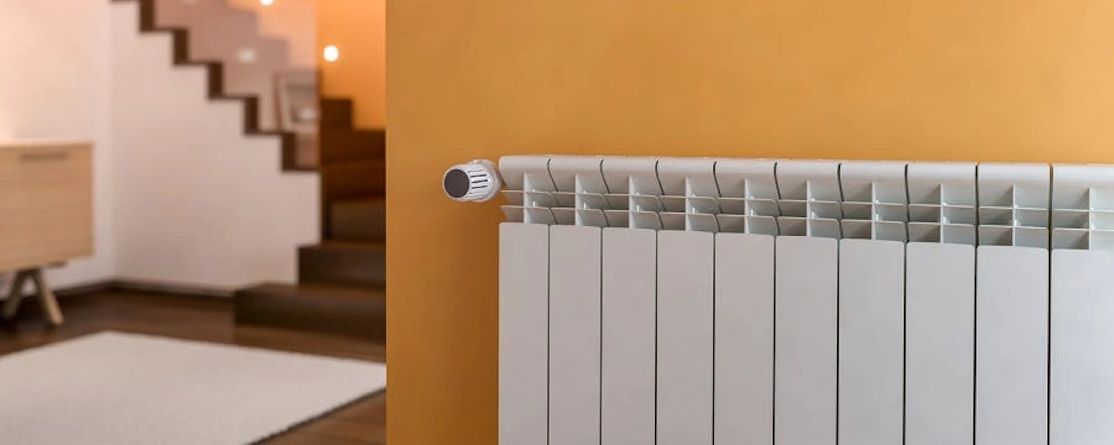 Radiateur blanc fixé sur un mur orange dans un couloir avec escalier