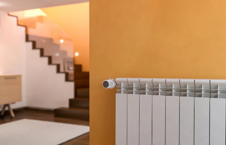 Radiateur blanc fixé sur un mur orange dans un couloir avec escalier
