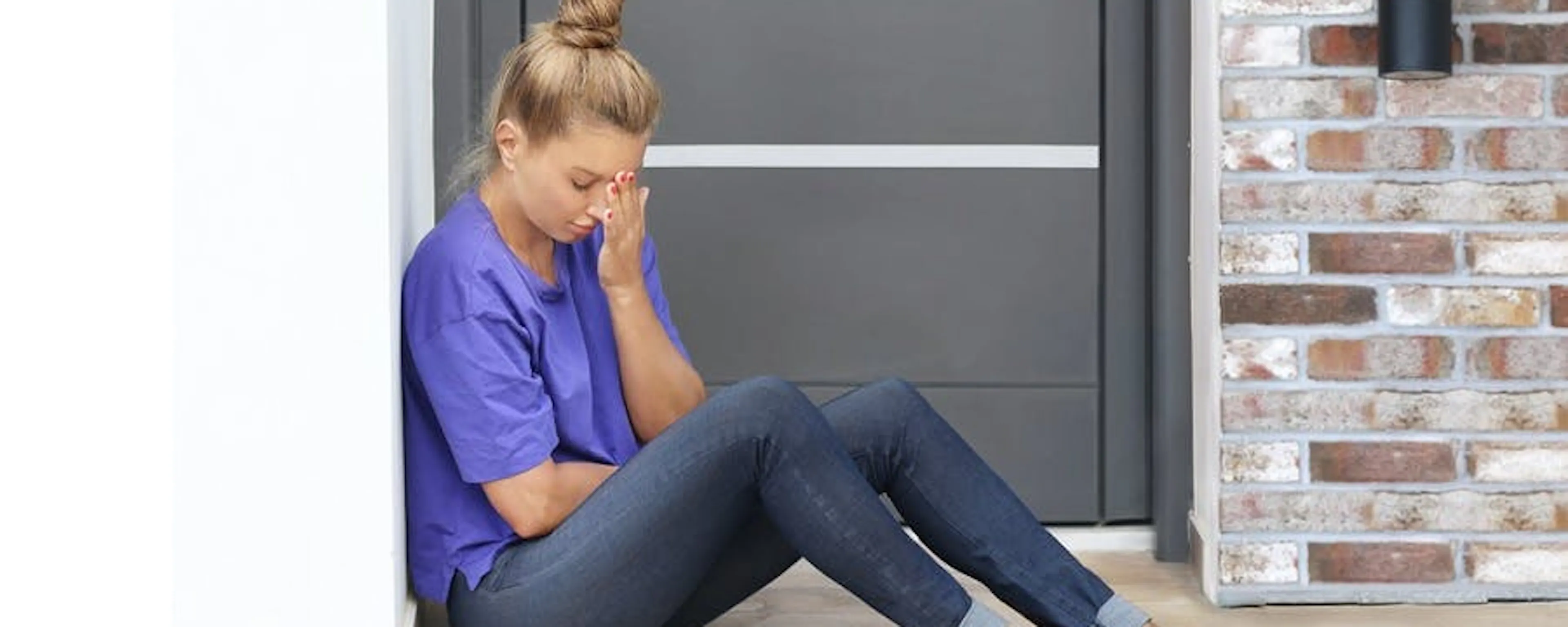 Femme assise devant sa porte d'entrée claquée, les mains sur le visage