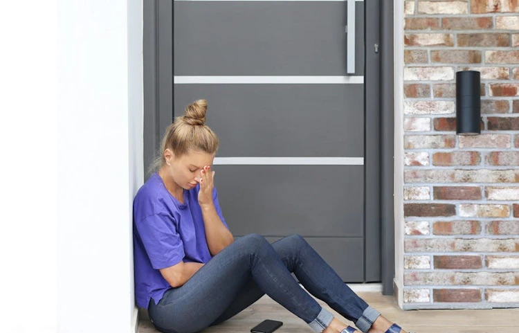 Femme assise devant sa porte d'entrée les mains sur le visage