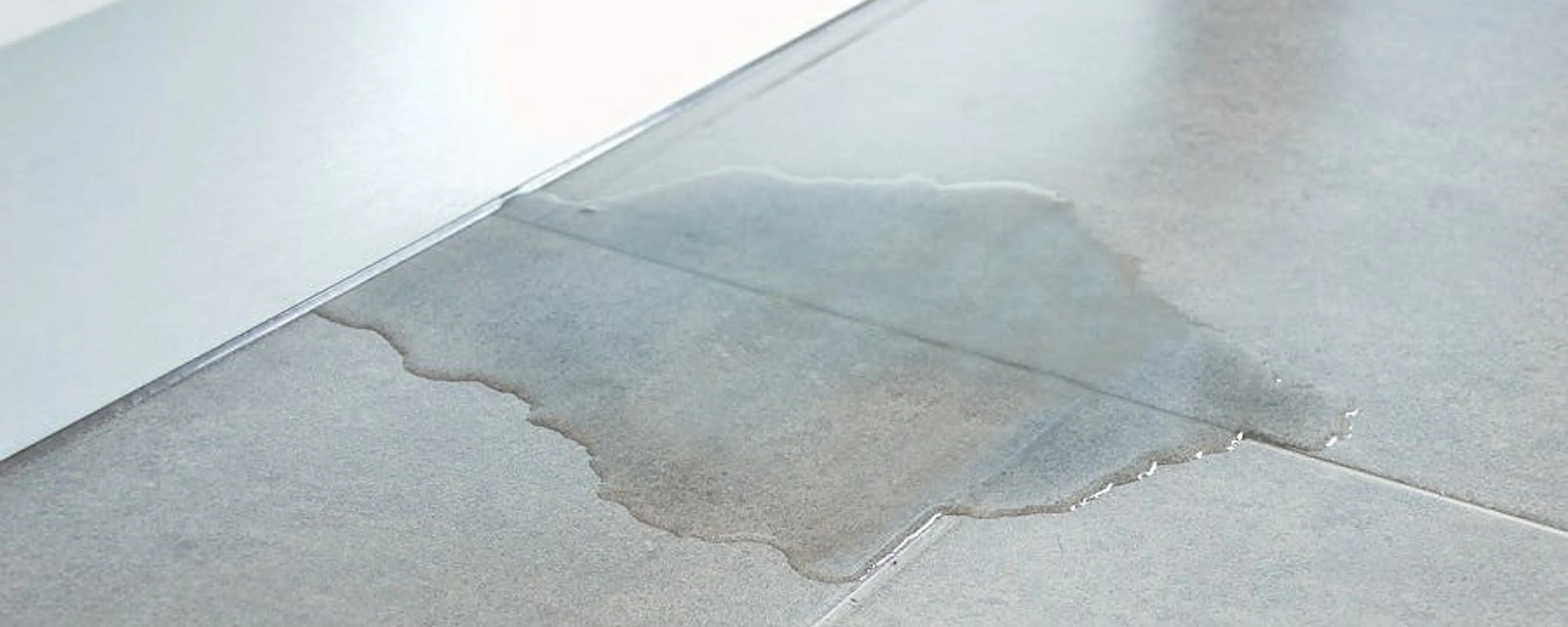 Flaque d'eau sur sol carrelé gris due à une fuite d'eau dans le sol