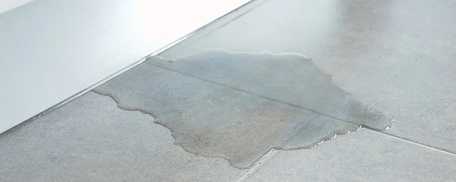 Flaque d'eau sur sol carrelé gris due à une fuite d'eau dans le sol