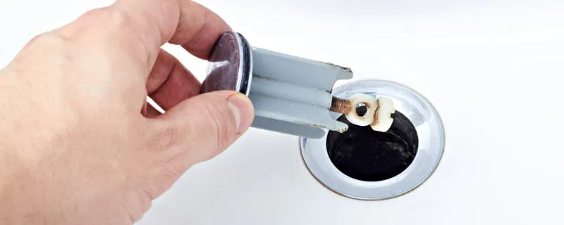 Main tenant le siphon chromé d'un lavabo afin de supprimer les mauvaises odeurs de la canalisation