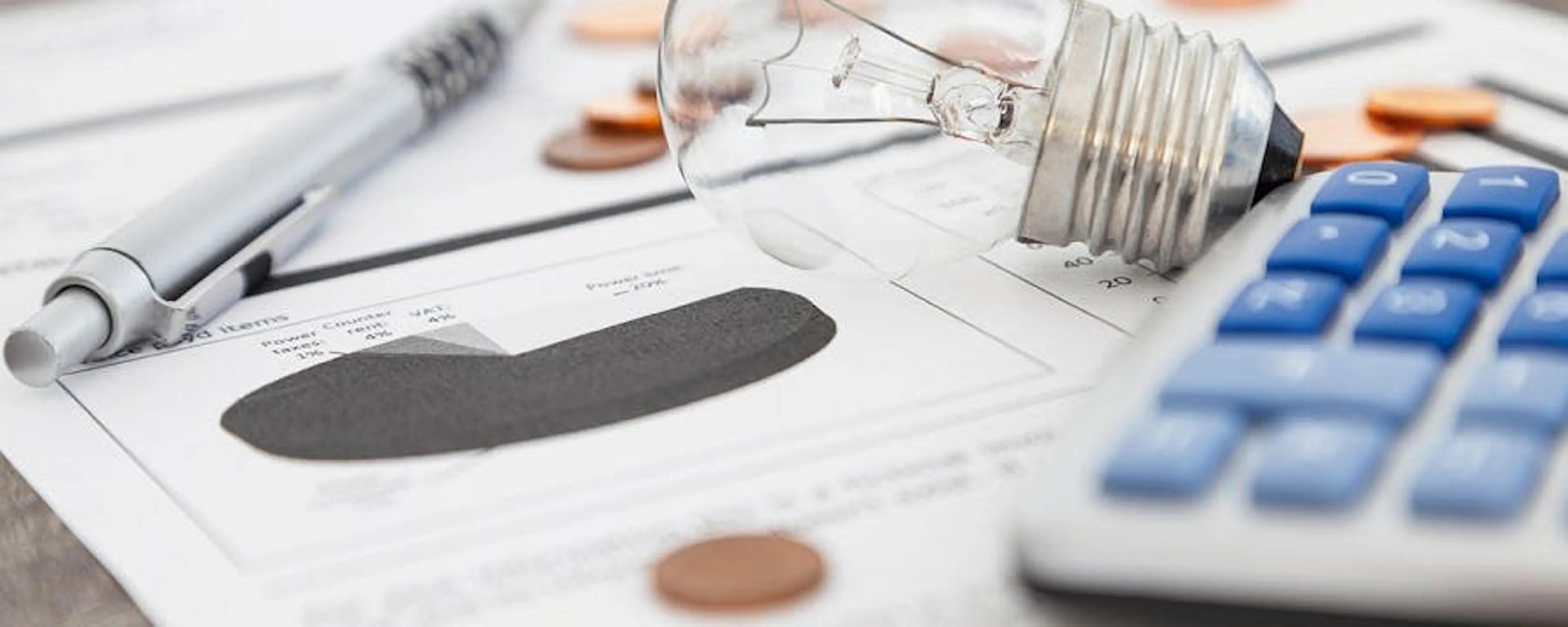 Ampoule, calculatrice et pièces de monnaie sur des documents afin de bien comprendre sa facture d'électricité