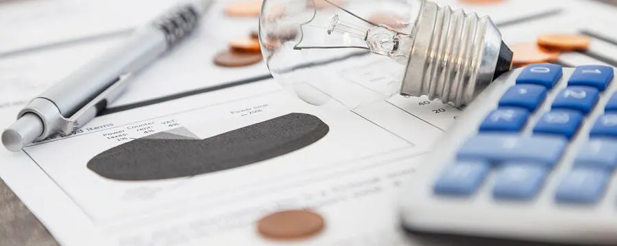Ampoule, calculatrice et pièces de monnaie sur des documents afin de bien comprendre sa facture d'électricité