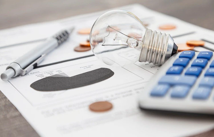 Ampoule, calculatrice et pièces de monnaie posées sur des documents financiers