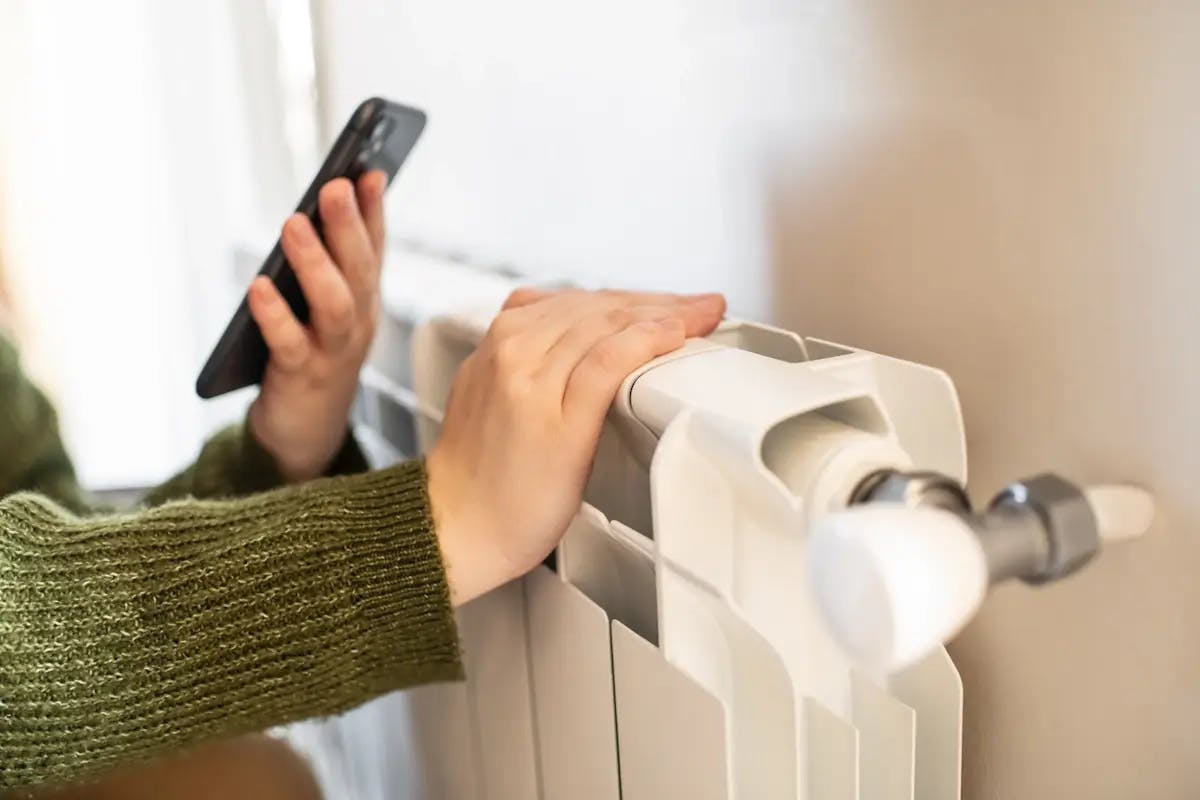 Main réglant le thermostat d'un radiateur blanc avec un smartphone