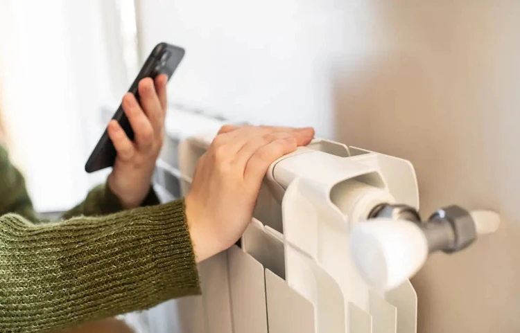 Main réglant le thermostat d'un radiateur blanc avec un smartphone