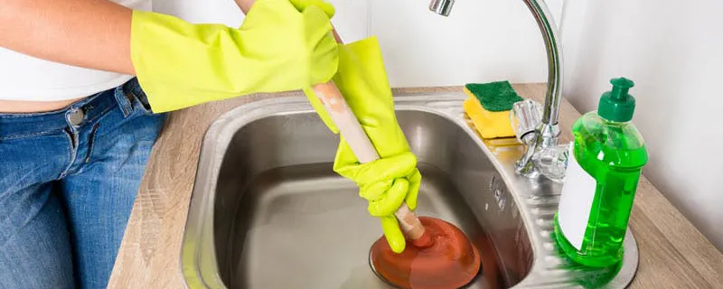 Mains gantées utilisant une ventouse pour déboucher une canalisation d'évier