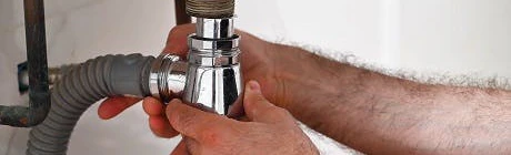 Plombier serrant le siphon sous un lavabo de salle de bain