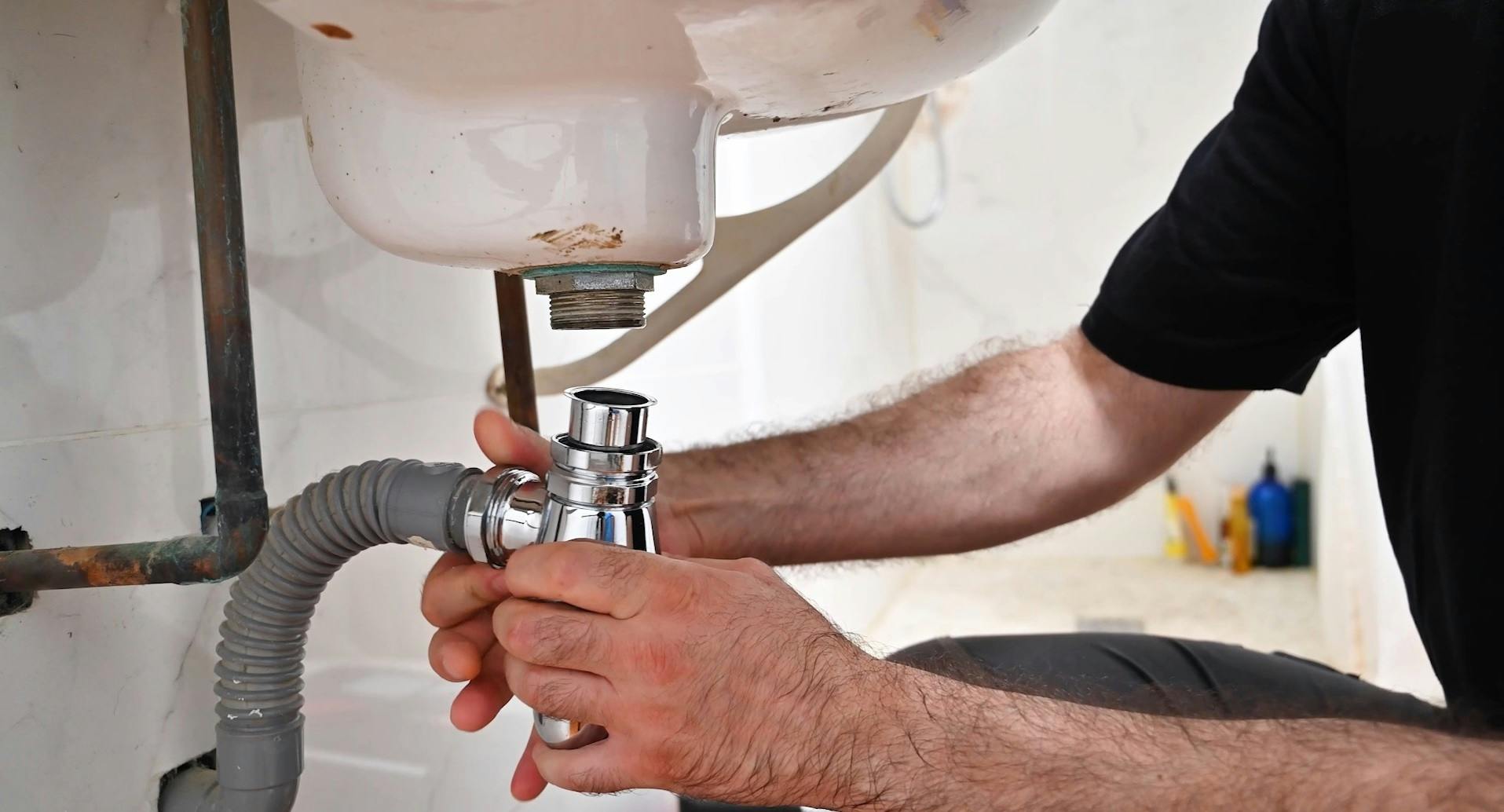 Technicien réparant la tuyauterie sous un lavabo blanc