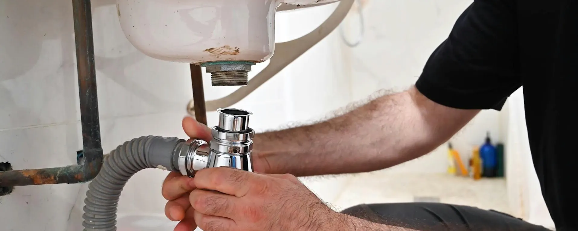 Technicien démontant le siphon et la tuyauterie sous un lavabo blanc