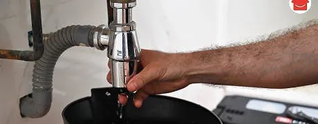 Main resserrant le raccord du siphon sous un lavabo