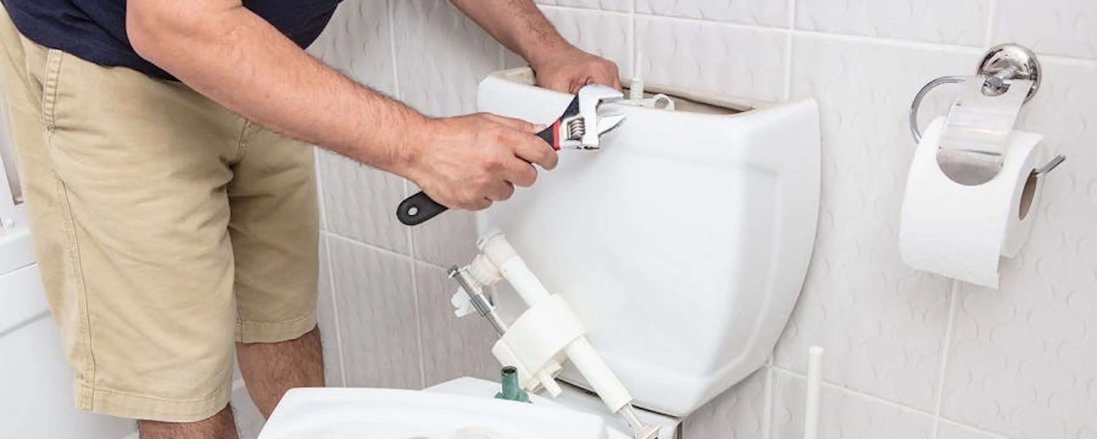 Homme réparant la chasse d'eau d'un WC avec une clé