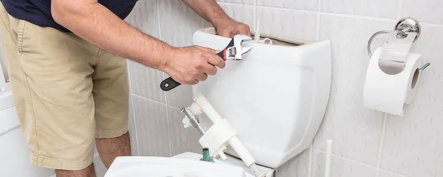 Homme réparant la chasse d'eau d'un WC avec une clé