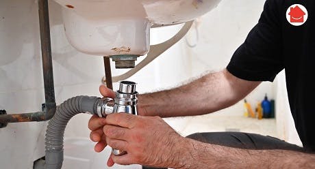 Plombier intervenant sur les tuyaux sous un évier de salle de bain