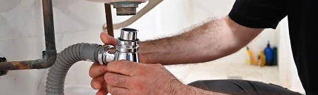 Plombier intervenant sur les tuyaux sous un évier de salle de bain