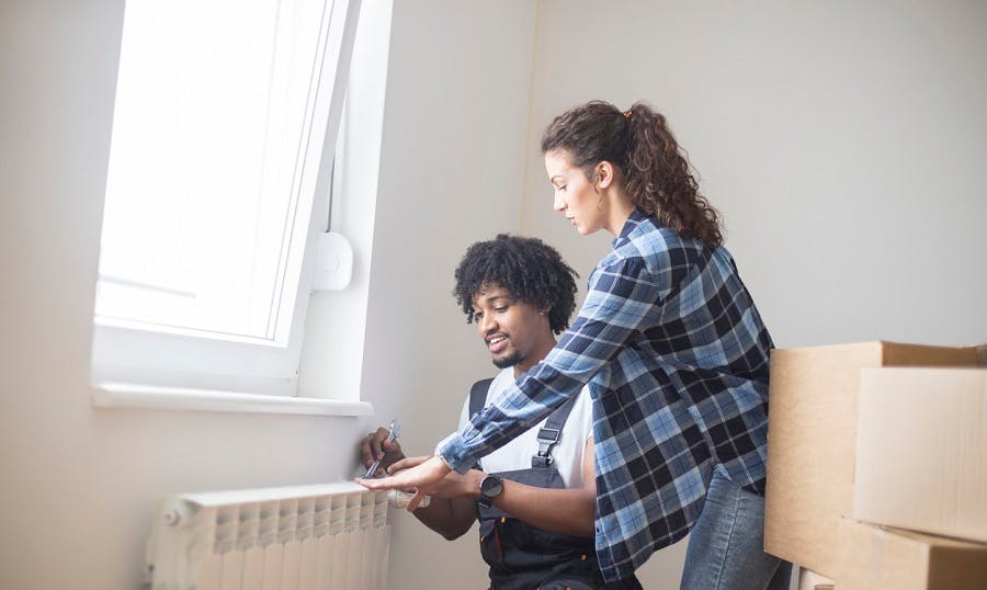 Couple regardant un radiateur blanc dans un appartement avec des cartons