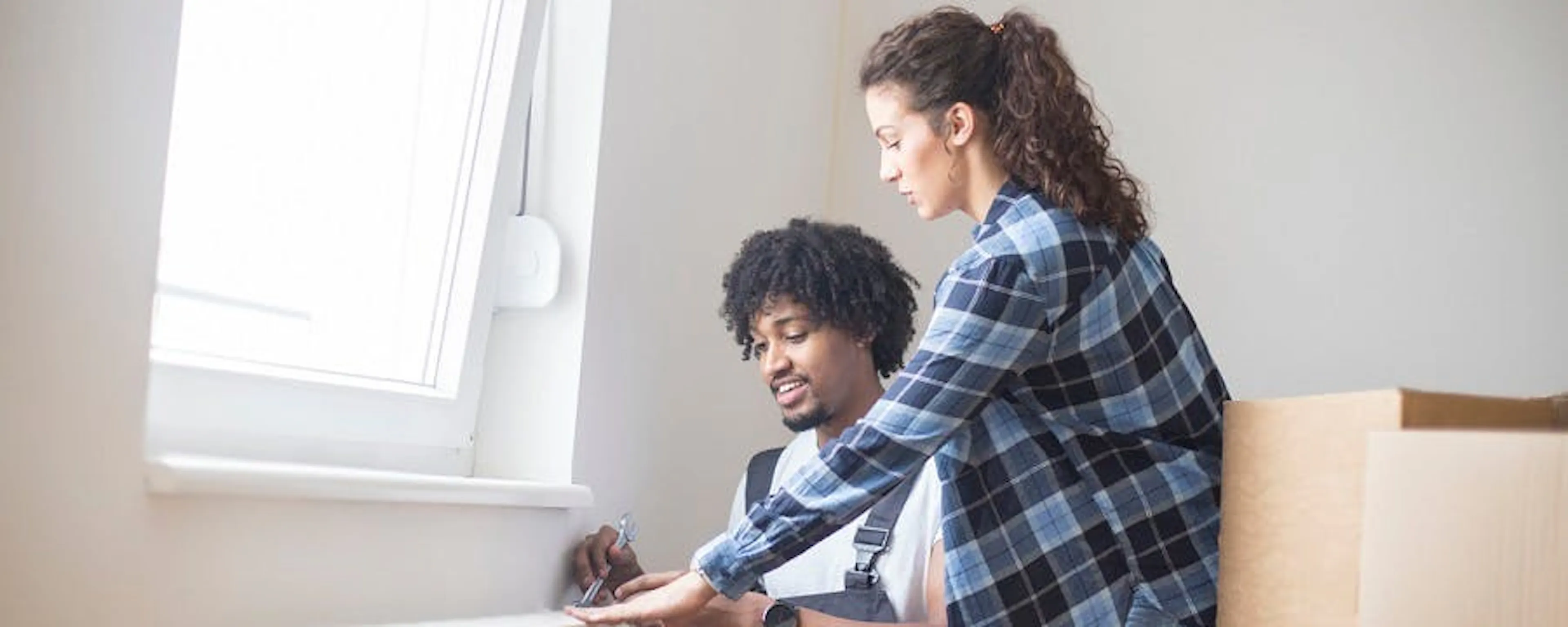 Couple devant un radiateur blanc à désembouer dans un appartement avec des cartons