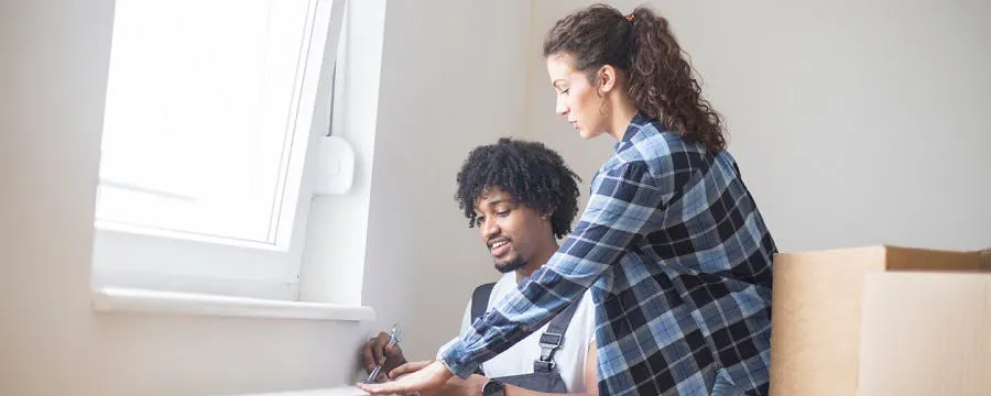 Couple devant un radiateur blanc à désembouer dans un appartement avec des cartons
