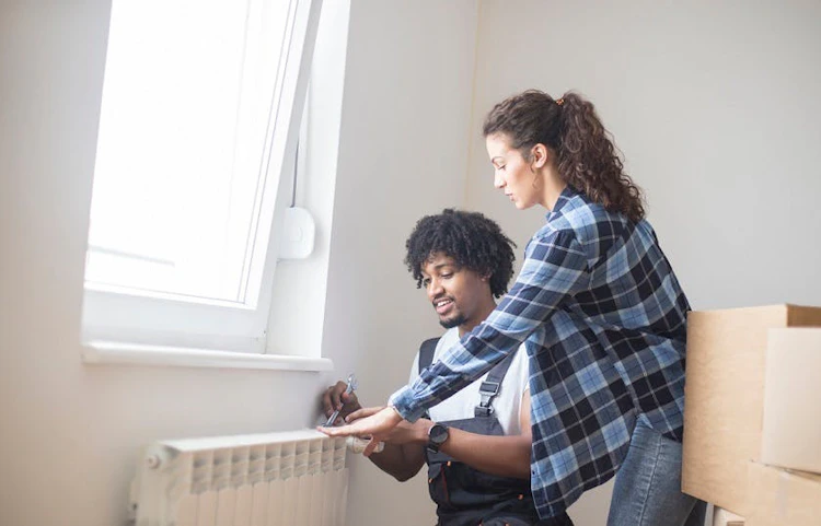 Couple regardant un radiateur blanc dans un appartement avec des cartons