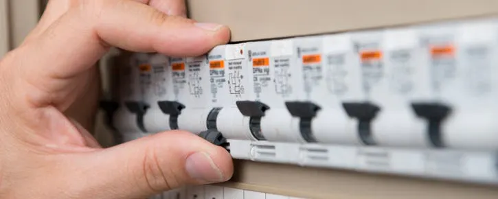 Main actionnant des disjoncteurs qui ont sauté dans un tableau électrique