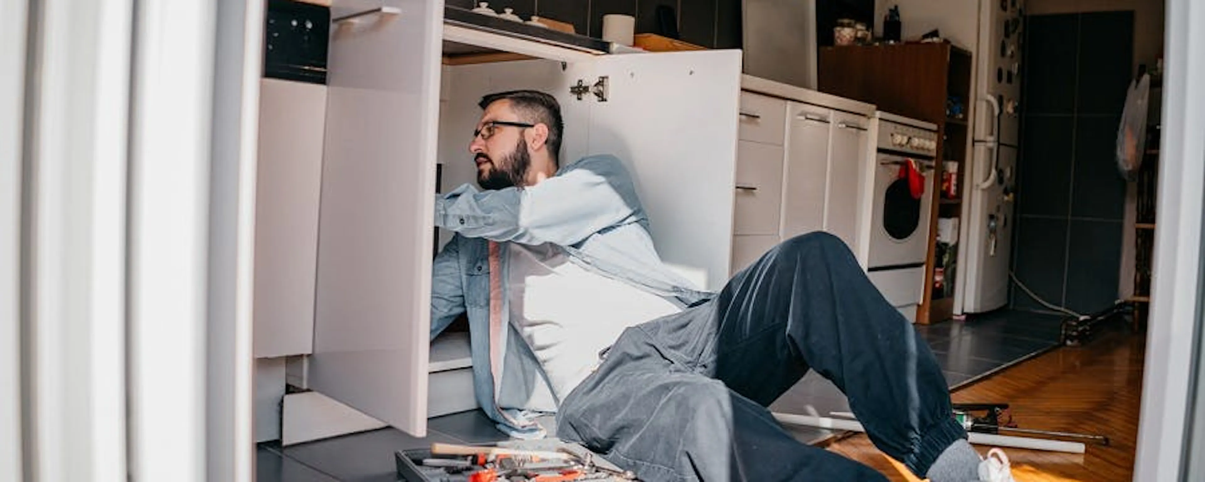 Homme allongé inspectant sous l'évier les canalisations où l'eau remonte, avec une boîte à outils