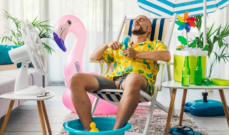 Homme en tenue estivale se rafraîchissant avec un ventilateur dans son salon