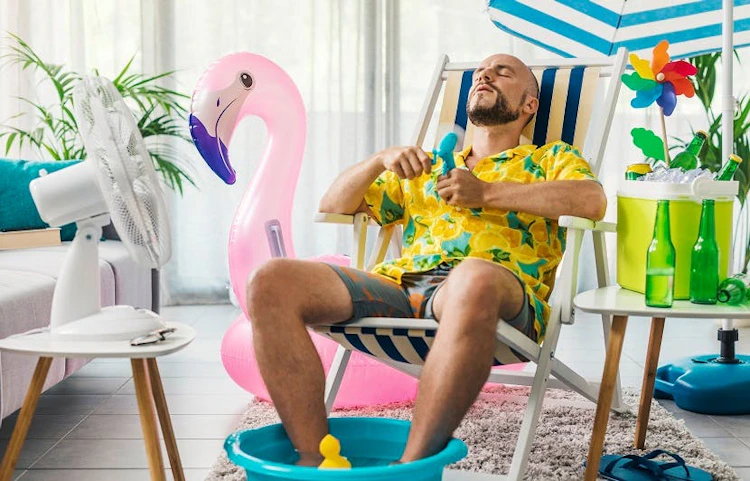 Homme en tenue estivale se rafraîchissant avec un ventilateur dans son salon